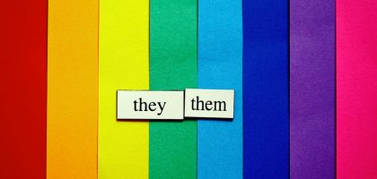 They/Them pronouns on rainbow-colored paper background.